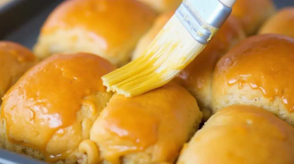 Applying a golden buttery glaze on top of breakfast sliders before baking.