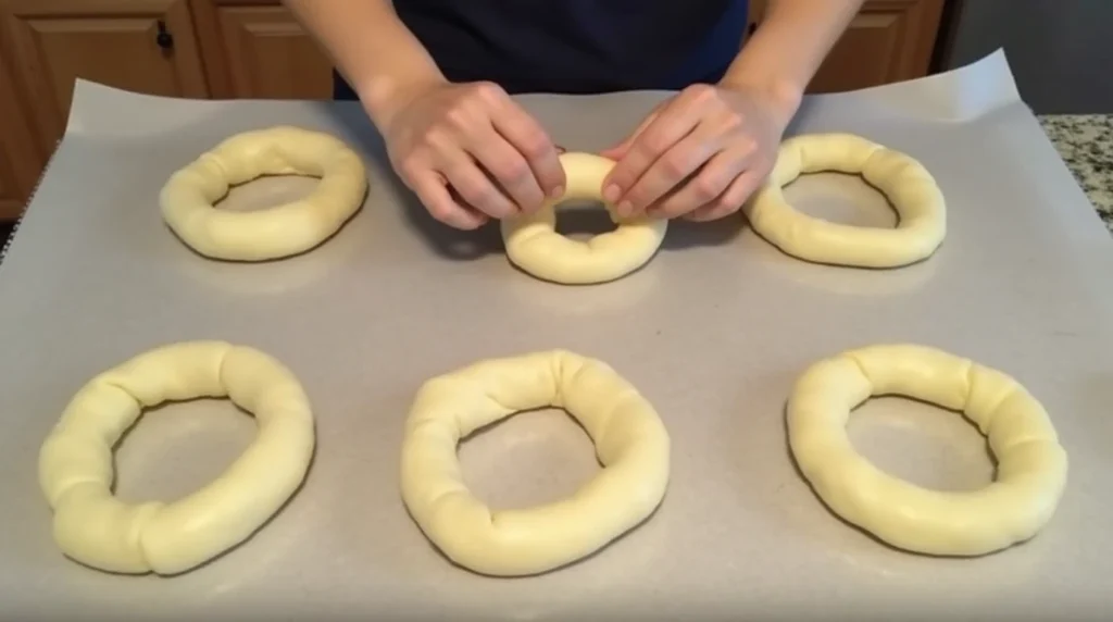 Shaping protein bagel dough into rings on a kitchen counter.